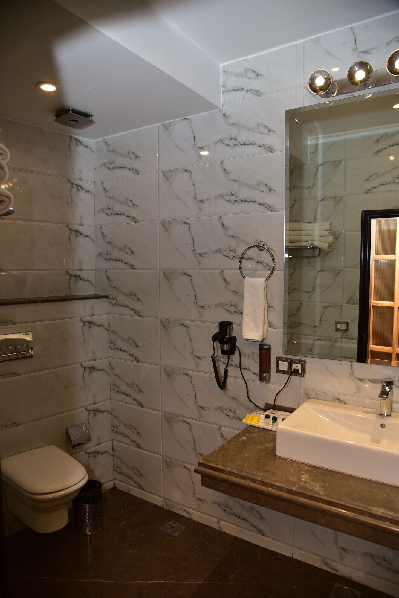 Un baño con pared de mármol, un lavamanos con espejo y un inodoro.