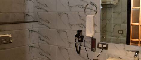 Un baño con pared de mármol, un lavamanos con espejo y un inodoro.