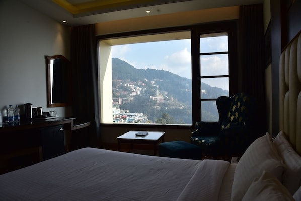 Habitación de hotel con cama, escritorio con silla, ventana y vista a la montaña, además de una barra de bar.