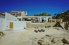 Ein modernes Strandhaus mit Steinwand, Holztür und Terrasse mit Liegestühlen.