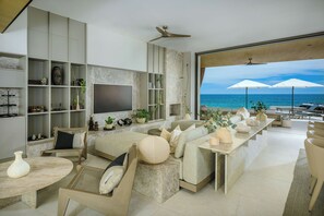 Ein modernes Wohnzimmer mit großem Fernseher, Sitzgelegenheiten und Blick auf den Ozean.