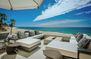 Eine Strandlounge mit weißen Sofas, gemusterten Kissen und einem großen Sonnenschirm.