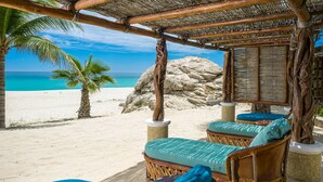 Een strandlounge met rieten meubels en kussens, met uitzicht op een zanderig strand en de oceaan.