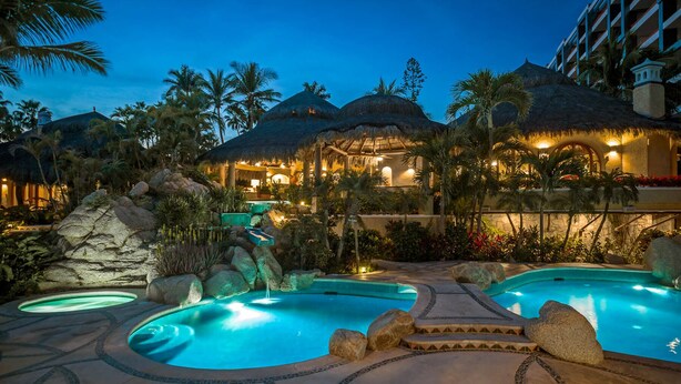 Een resort met meerdere zwembaden, bungalows met rieten daken en weelderige tropische beplanting.