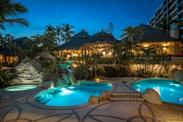 Ein Resort mit mehreren Pools, strohgedeckten Gebäuden und üppiger tropischer Bepflanzung.
