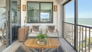 Un balcone con vista sull'oceano, una ventola a soffitto e un’area salotto con tavolo e sedie.