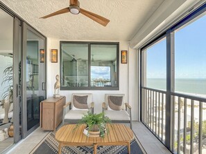 Ein Balkon mit Blick auf das Meer, ein Deckenventilator und eine Sitzecke mit Tisch und Stühlen.