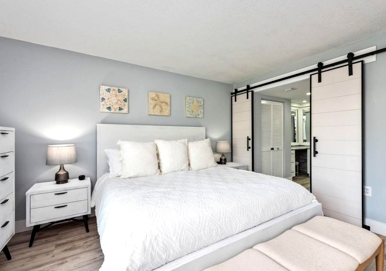 A bedroom with a bed, nightstands, a bench, and a sliding closet door.