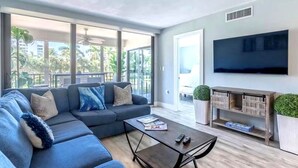 Ein modernes Wohnzimmer mit einer Eckcouch, einem Couchtisch, einem Flachbildfernseher und einem Balkon mit Pflanzen.