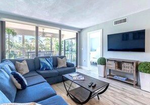 Ein modernes Wohnzimmer mit einer Eckcouch, einem Couchtisch, einem Flachbildfernseher und einem Balkon mit Pflanzen.