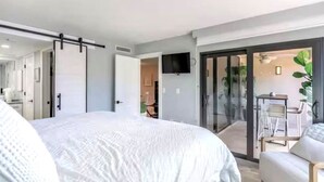 Ein modernes Schlafzimmer mit einem großen Bett, einer Schiebetür zum Balkon und einem an der Wand befestigten Fernseher.