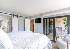 Ein modernes Schlafzimmer mit einem großen Bett, einer Schiebetür zum Balkon und einem an der Wand befestigten Fernseher.