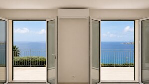 Una habitación con un amplio ventanal corredera que da a un balcón con vistas al mar.