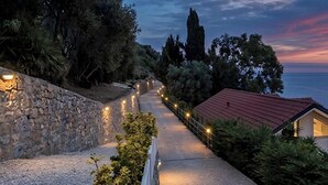 Un sendero pavimentado bordeado de vegetación y muros de piedra, que conduce a un edificio con techo rojo.