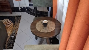 A room with a round table, a chair, a small table with a fan, and a decorative rug. - Makey Holiday Homes Diani (Diani Beach)