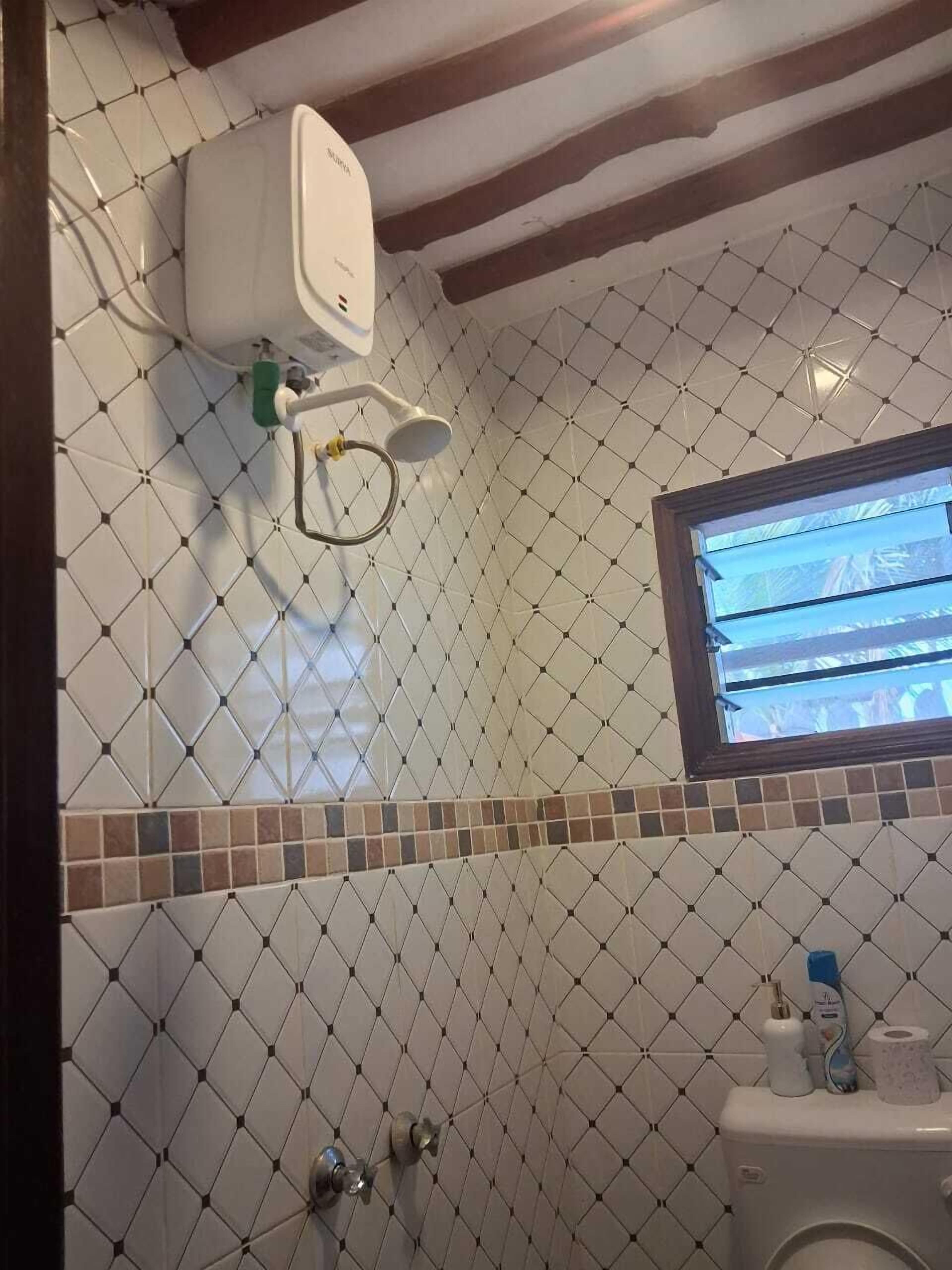 Un baño con pared de azulejos, una ventana, ducha y retrete.