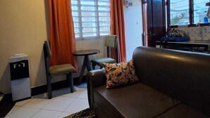 A room with a sofa, a small table, a chair, a water dispenser, and a window with curtains. - Makey Holiday Homes Diani (Diani Beach)