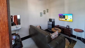 A living room with a sofa, a television, a small table, a refrigerator, and a sink. - Makey Holiday Homes Diani (Diani Beach)