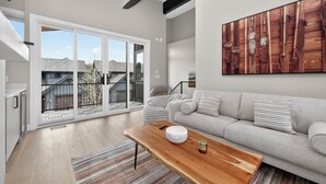 Een ruime woonkamer met een grote schuifpui naar een balkon, een grijze bank, een houten salontafel en een plafondventilator.