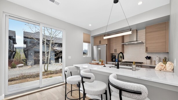 Een moderne keuken met een groot eiland, barstoelen en een uitzicht door glazen deuren.