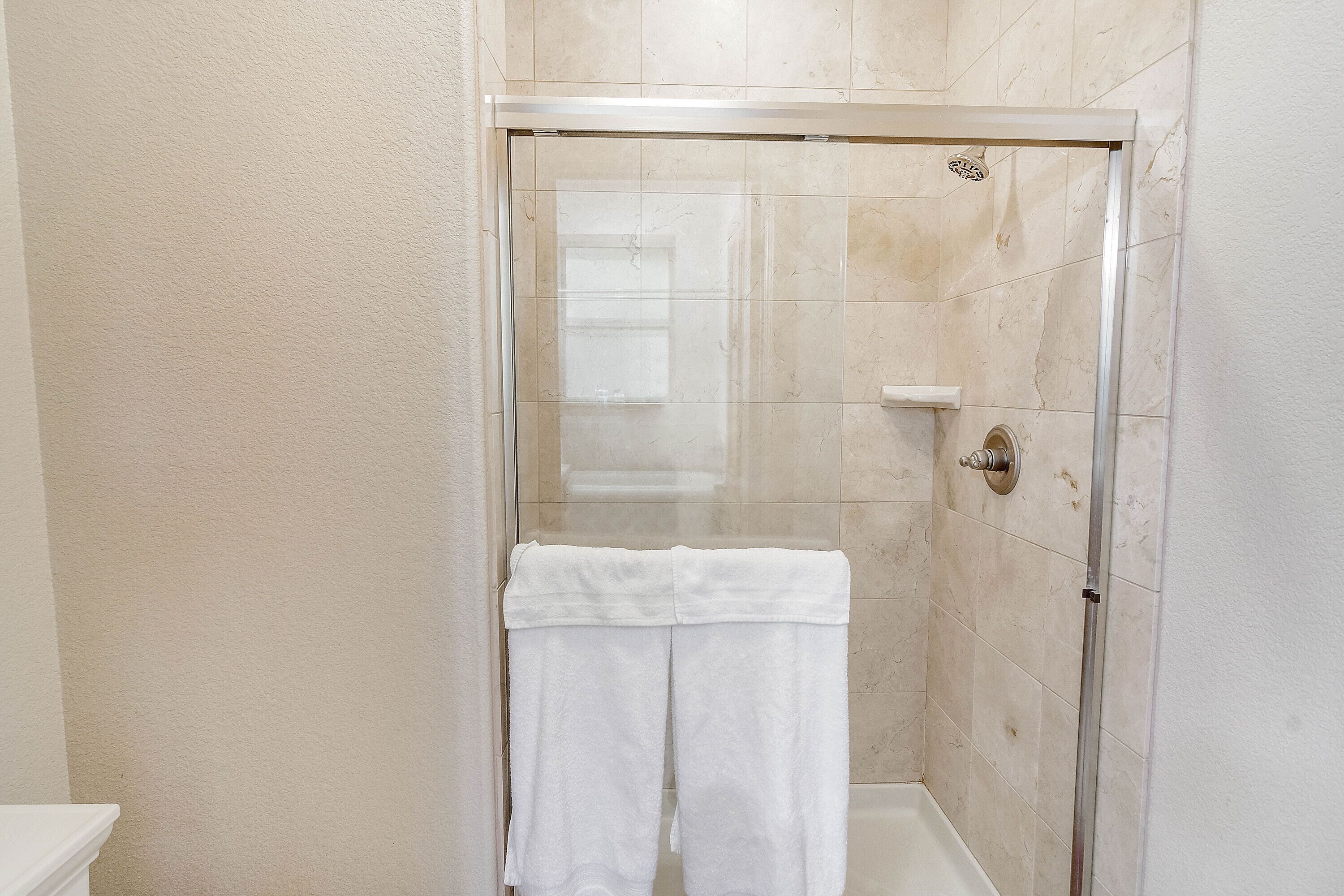 A bathroom with a glass-enclosed shower, a white towel hanging on the wall, and a toilet.