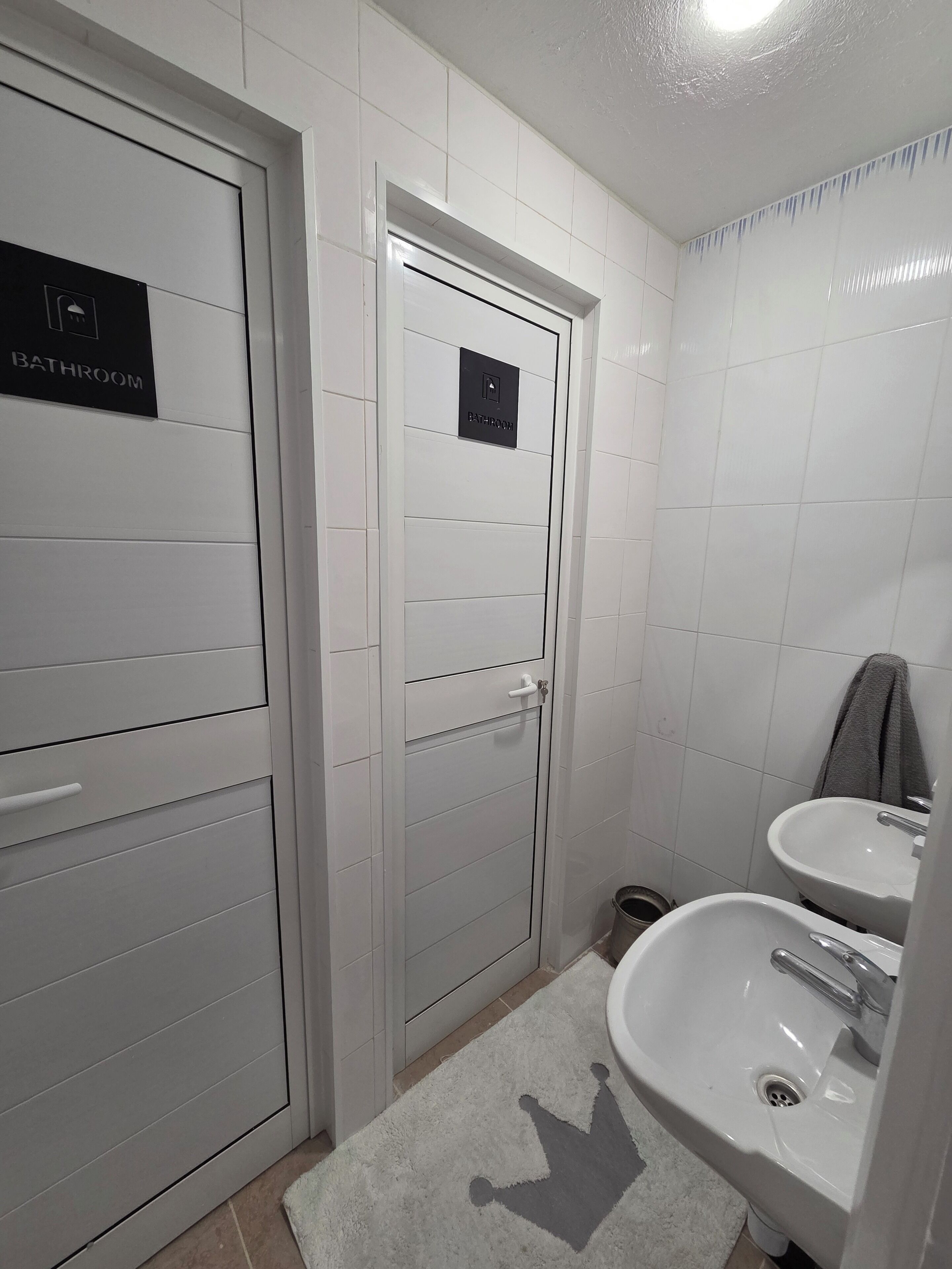 Een badkamer met twee wasbakken, een handdoekhouder en een deur met de tekst 'BATHROOM'.
