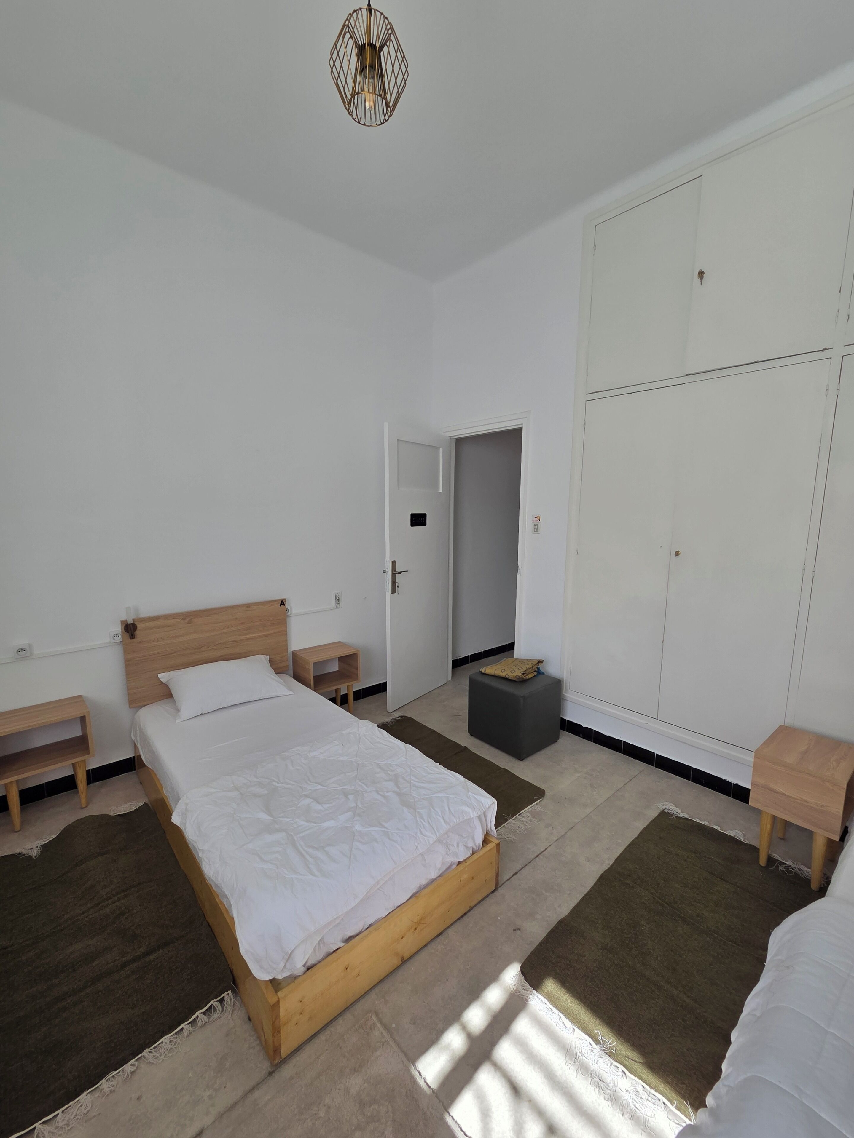Un dormitorio con cama, mesitas de noche, armario y una puerta que da a otra habitación.