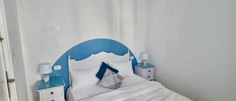 A bedroom with a bed, a chandelier, two bedside tables with lamps, and a door.