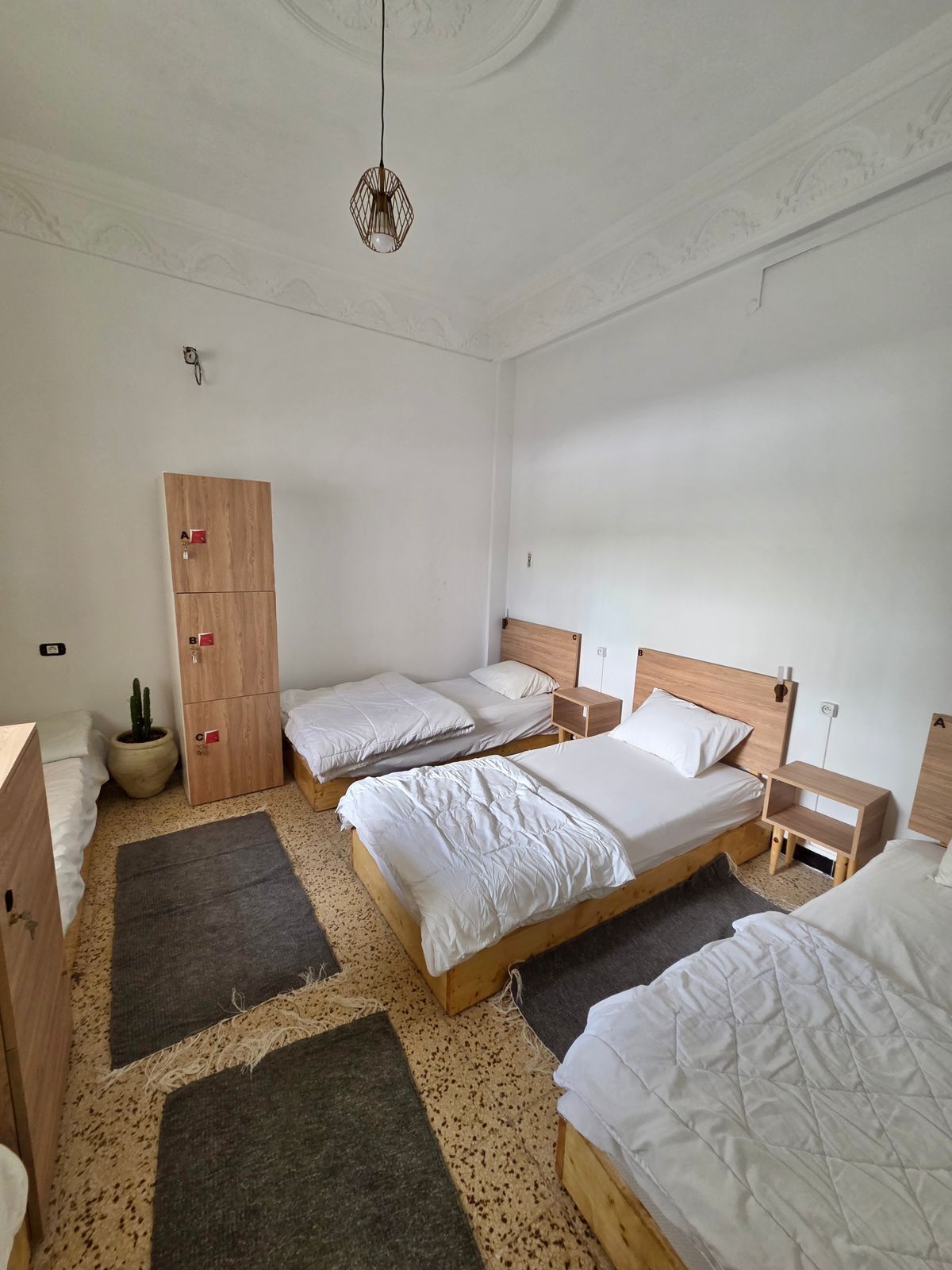 Een kamer met drie bedden, een garderobe, een hanglamp en een kleine potplant.