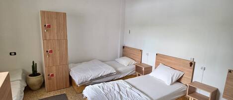 A room with three beds, a wardrobe, a hanging light fixture, and a small potted plant.