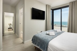 Hotelkamer met een bed, een flatscreen televisie, een groot raam met uitzicht op zee en een deur naar een badkamer.