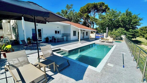 Uma piscina com espreguiçadeiras, um alpendre coberto e um edifício branco com telhado vermelho.