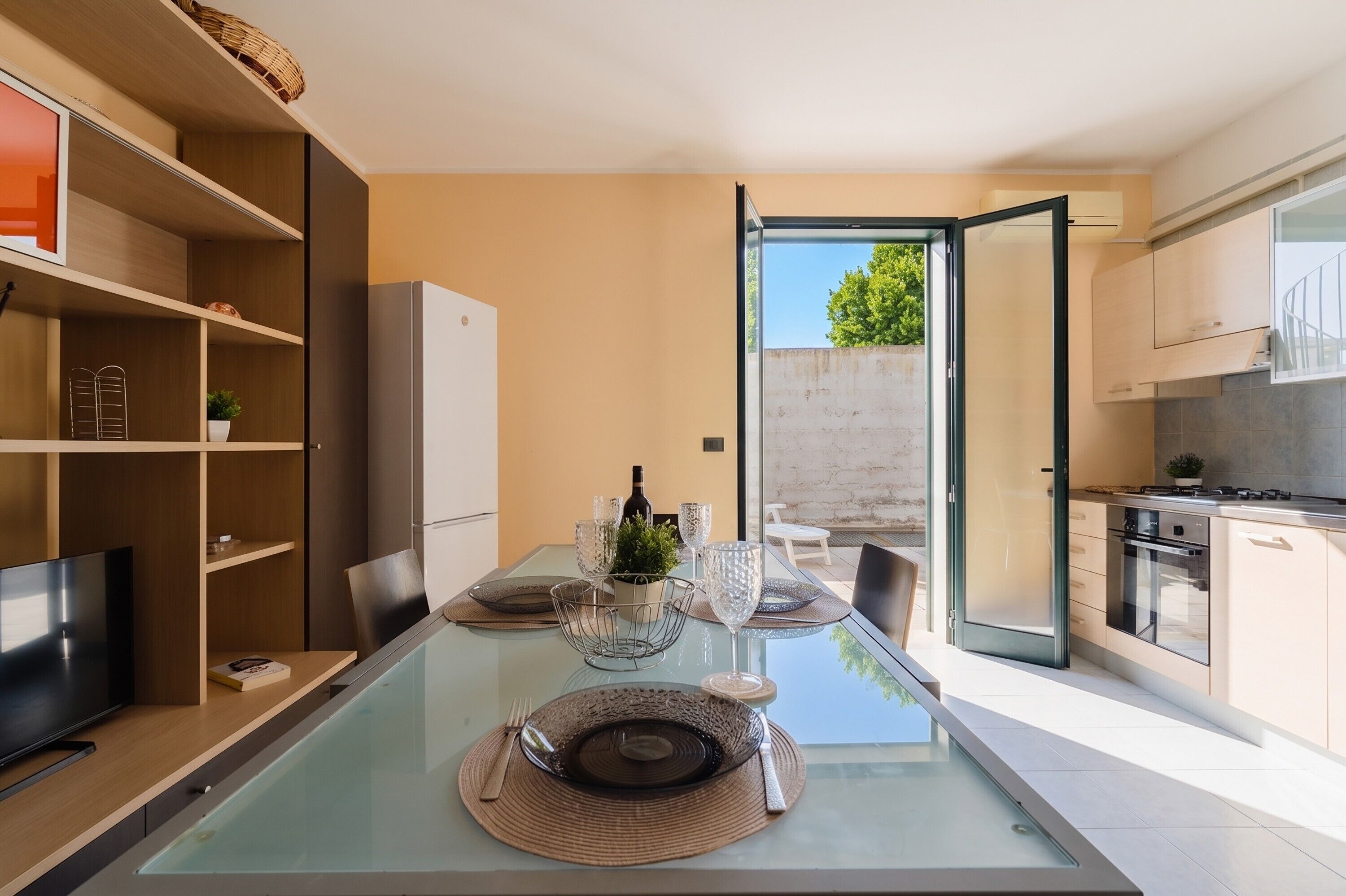 A modern kitchen with a dining area, a TV, and a view of the outdoors.