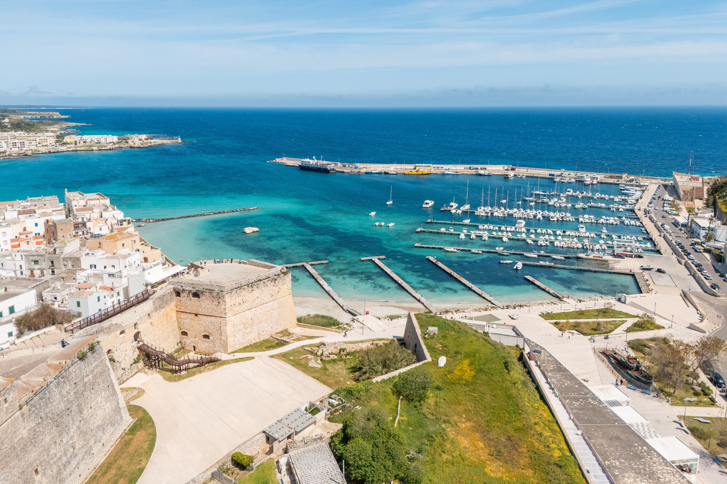 Uma cidade costeira com um porto de iates, uma fortaleza histórica e vista clara para o mar.