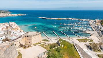 Uma cidade costeira com um porto de iates, uma fortaleza histórica e vista clara para o mar.