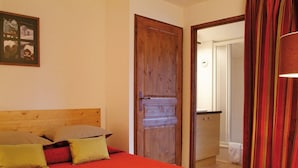 A bedroom with a wooden headboard, a bed with red bedding, a door leading to a bathroom, and a striped curtain. - Inviting Mountain Studio in Savoie (Brides-les-Bains)