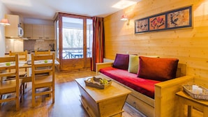 A wooden interior with a sofa, dining table, chairs, and a kitchen area. - Inviting Mountain Studio in Savoie (Brides-les-Bains)