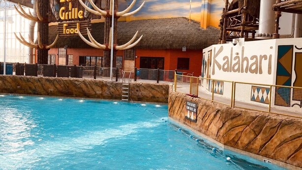 Area piscina interna con un cartello che indica 'Kalahari Grill Food' e un cartello con la scritta 'Non arrampicarsi sulle rocce'.