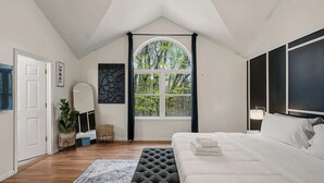 Una camera da letto con un letto grande, una finestra con tende, uno specchio e una pianta.