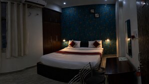 Quarto de hotel com cama, escrivaninha, cadeira, televisão e janela com cortinas.
