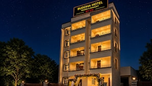 Un hotel de varios pisos con balcones, un letrero que indica que es un Buddha Hotel y una entrada bien iluminada.