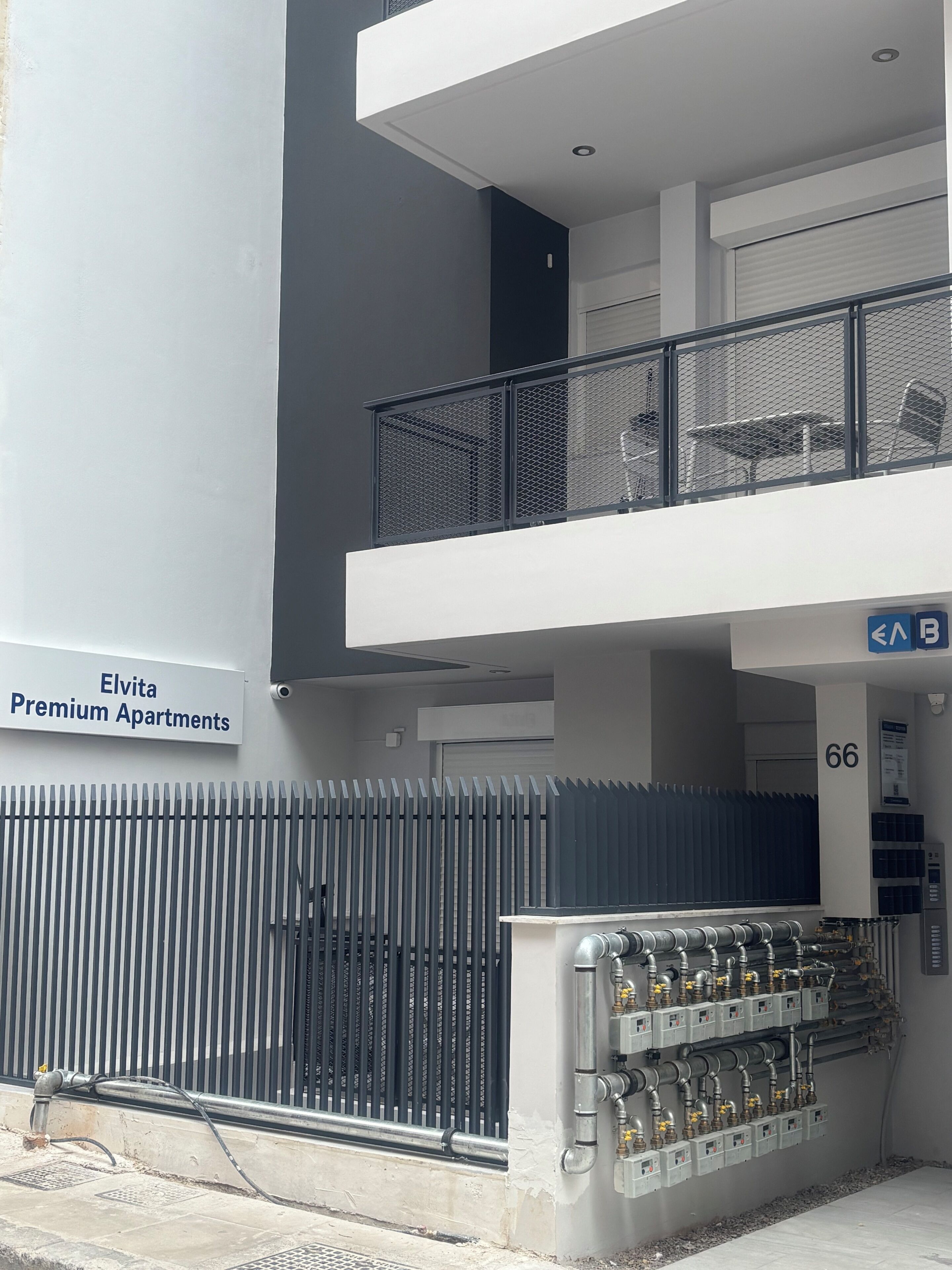 En bygning med skilt for 'Elvita Premium Apartments', en lukket indgang og et område med rør og ventiler.