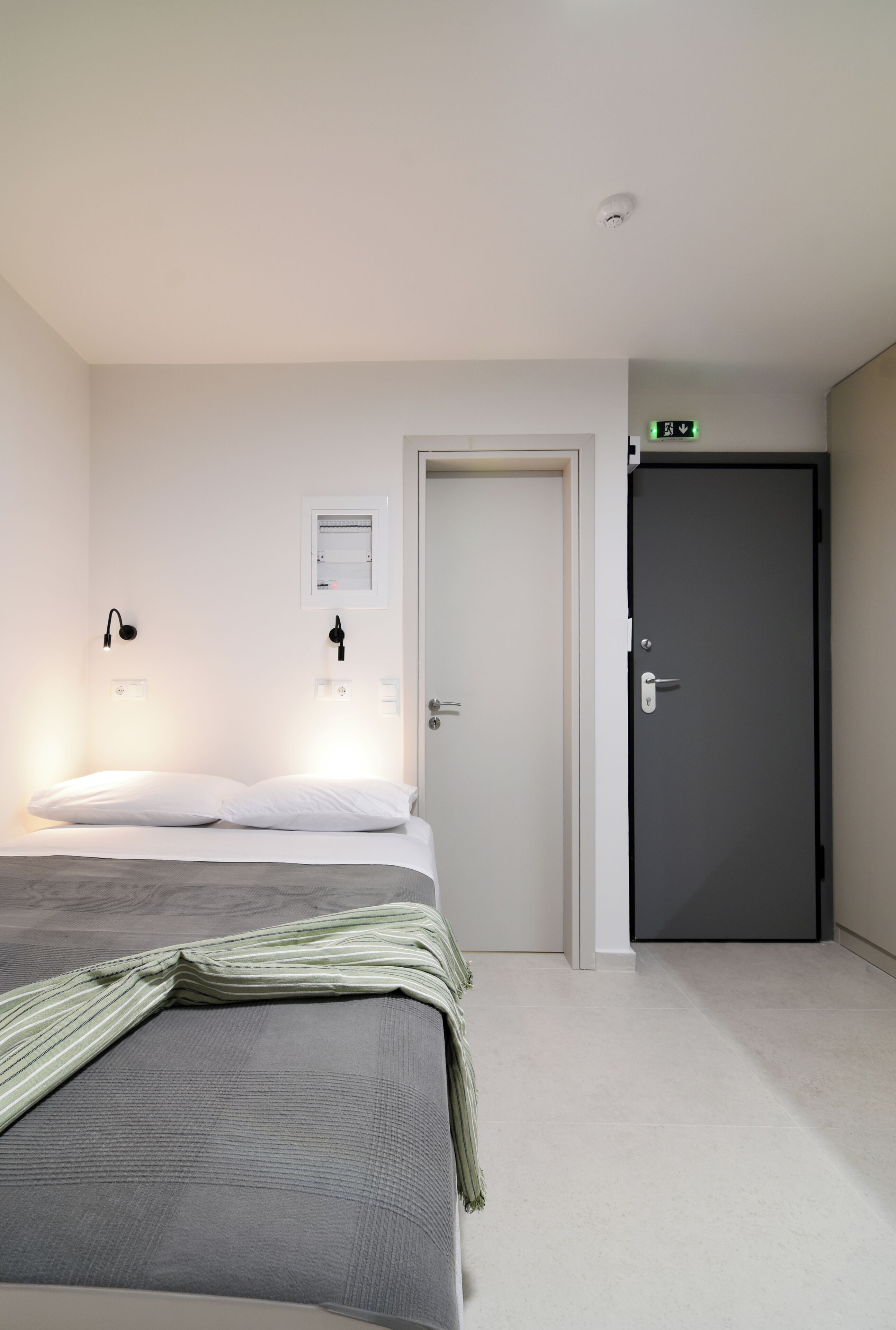 A bedroom with a bed, a door, and a wall-mounted light fixture.