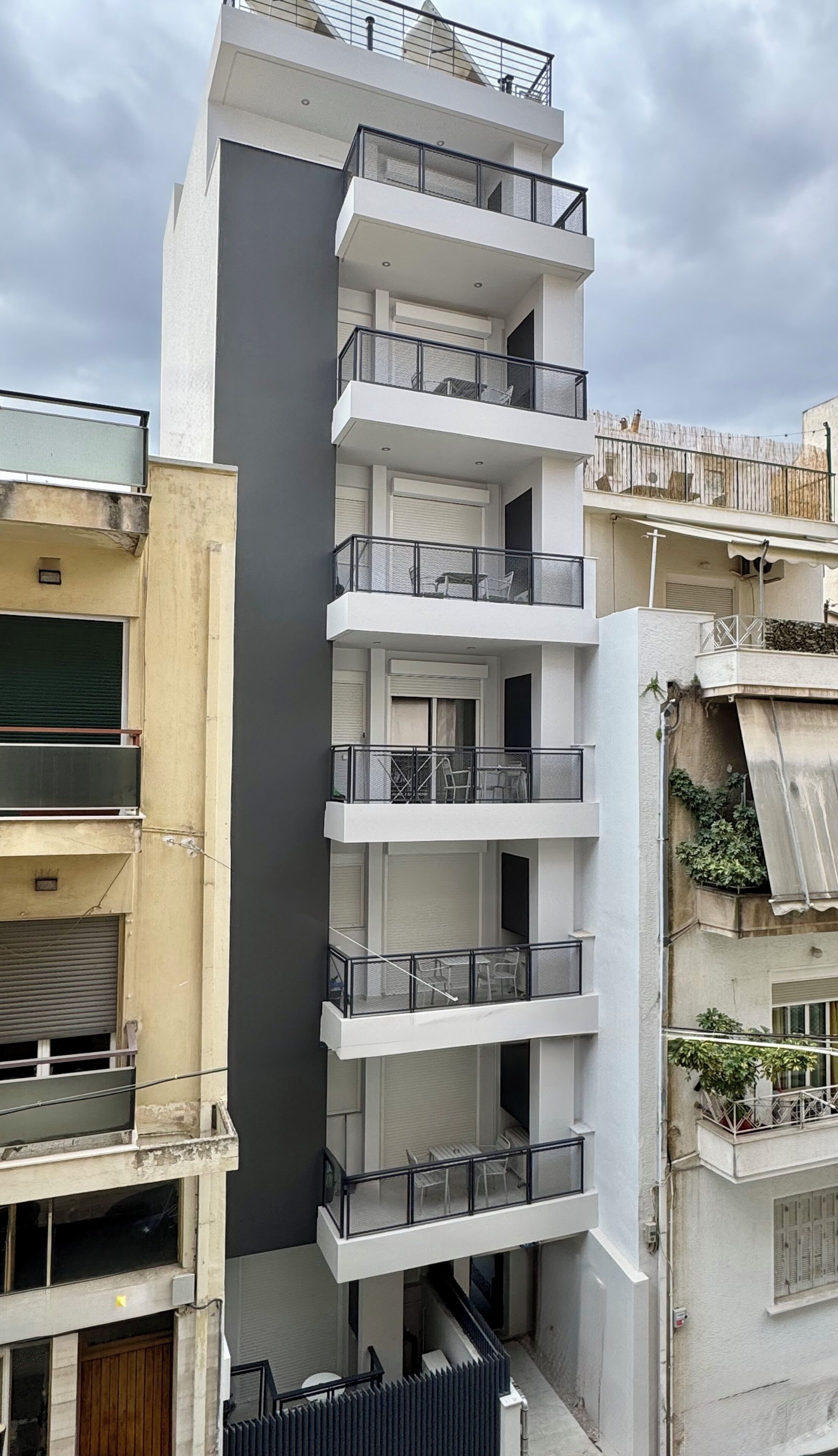 A multi-story building with balconies, a grey facade, and a window with a shutter.