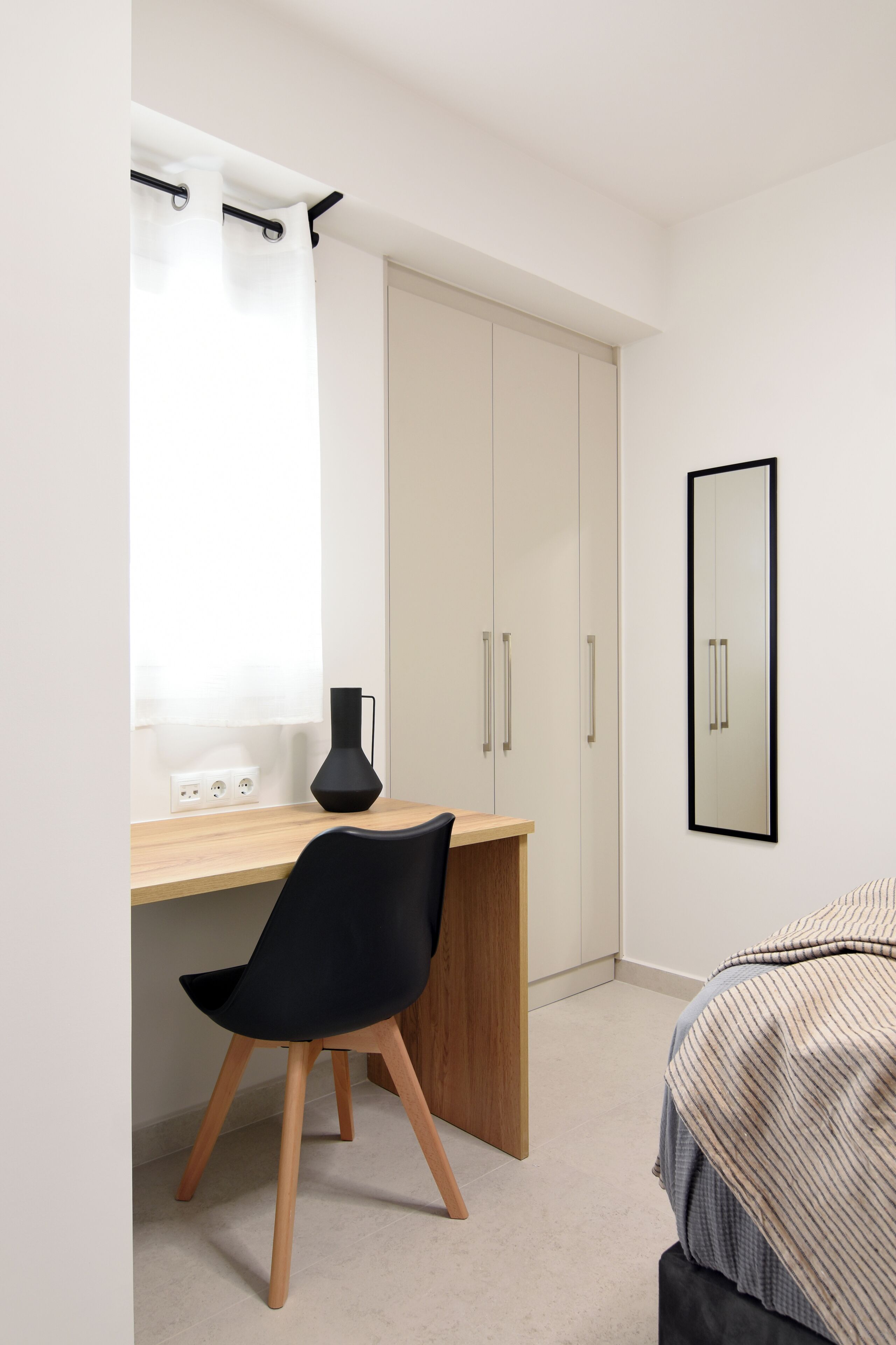 Um quarto com cama, escrivaninha, cadeira, guarda-roupa e espelho na parede.