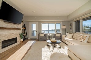 Ein Wohnzimmer mit Kamin, Flachbildfernseher, Sofa, Couchtisch und Blick ins Freie.