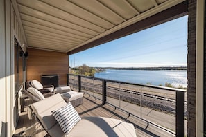 Eine überdachte Terrasse mit Liegestühlen und Blick auf einen See und Bahngleise.