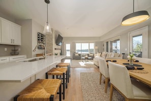 Eine moderne Küche mit Kochinsel, Essbereich mit Holztisch und Stühlen sowie ein Wohnbereich mit Sofa und Couchtisch.