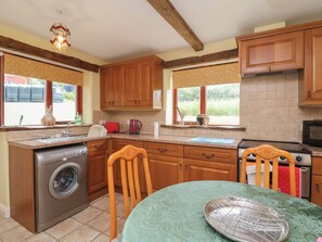 A kitchen with wooden cabinets, a washing machine, a table with a green tablecloth, and a stove. - The Retreat (Wellington)