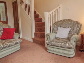A living room with a staircase, two patterned armchairs, and a red pillow. - The Retreat (Wellington)